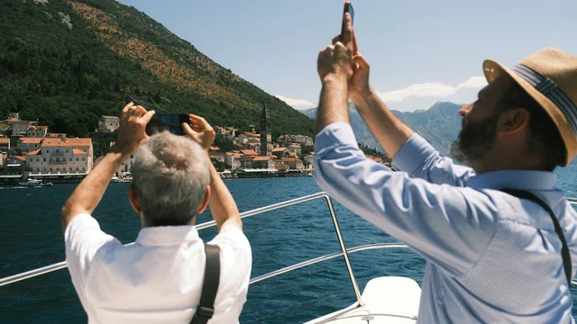 Two visitors photograph a coastal town from a boat